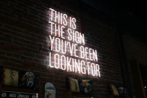 White neon sign reading "This is the sign you've been looking for" mounted on a brick wall